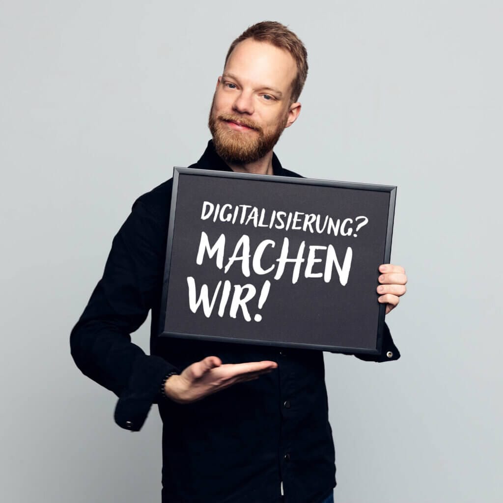 Marcel Drosse, Marketing Manager, mittleren Alters, lächelnd, mit einem Schild in der Hand auf dem „never gonna give you up“ drauf steht"