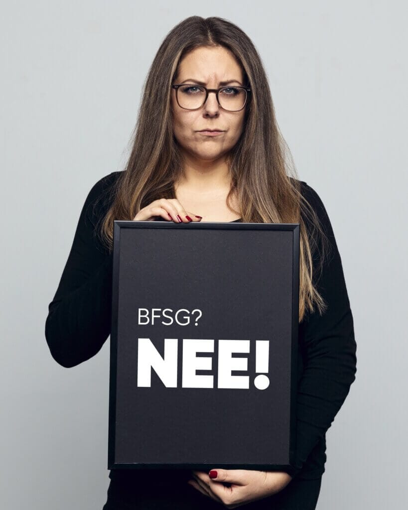 Frau mit ernstem Blick hält ein schwarzes Schild mit der Aufschrift „BFSG? NEE!“ – ein augenzwinkernder Einstieg in das Thema digitale Barrierefreiheit.