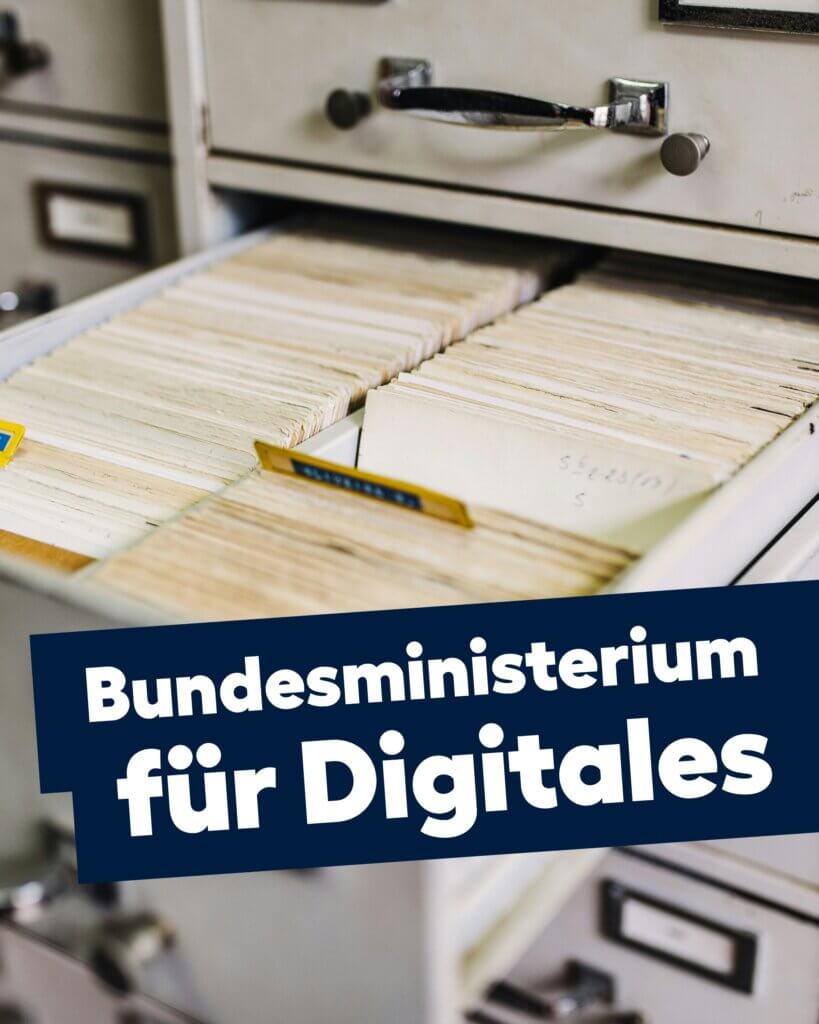 Ein offenes Karteikartenarchiv mit vielen Papierakten. Darüber liegt ein dunkelblauer Schriftbalken mit weißem Text: „Bundesministerium für Digitales“.