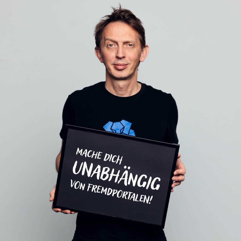 Marcel Drosse, Marketing Manager, mittleren Alters, lächelnd, mit einem Schild in der Hand auf dem „never gonna give you up“ drauf steht"